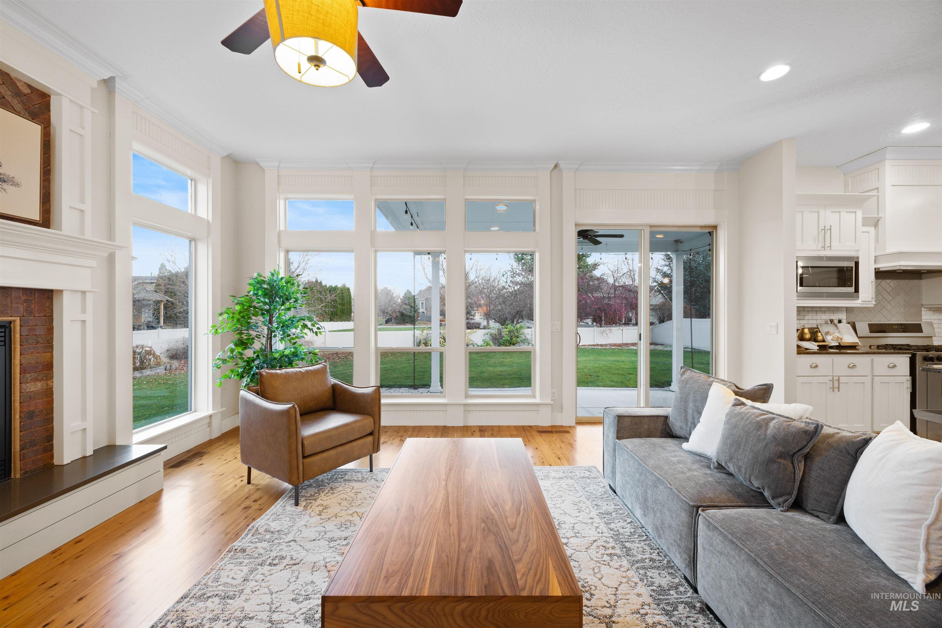 Living room featuring ceiling fan, a glass covered fireplace, plenty of natural light, light wood-type flooring, and ornamental molding