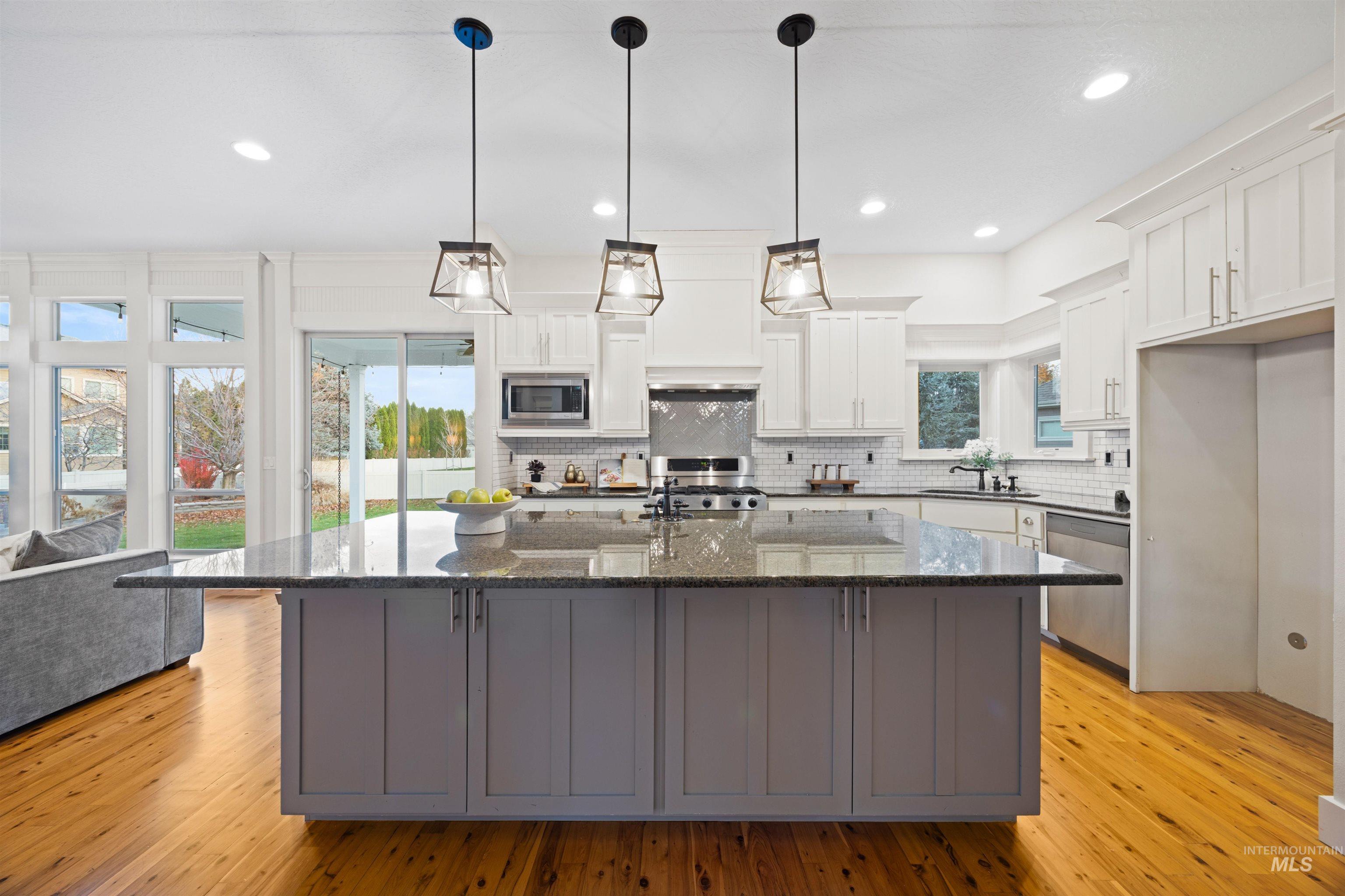 Kitchen with gray cabinets, white cabinets, dark stone countertops, an island with sink, and decorative light fixtures