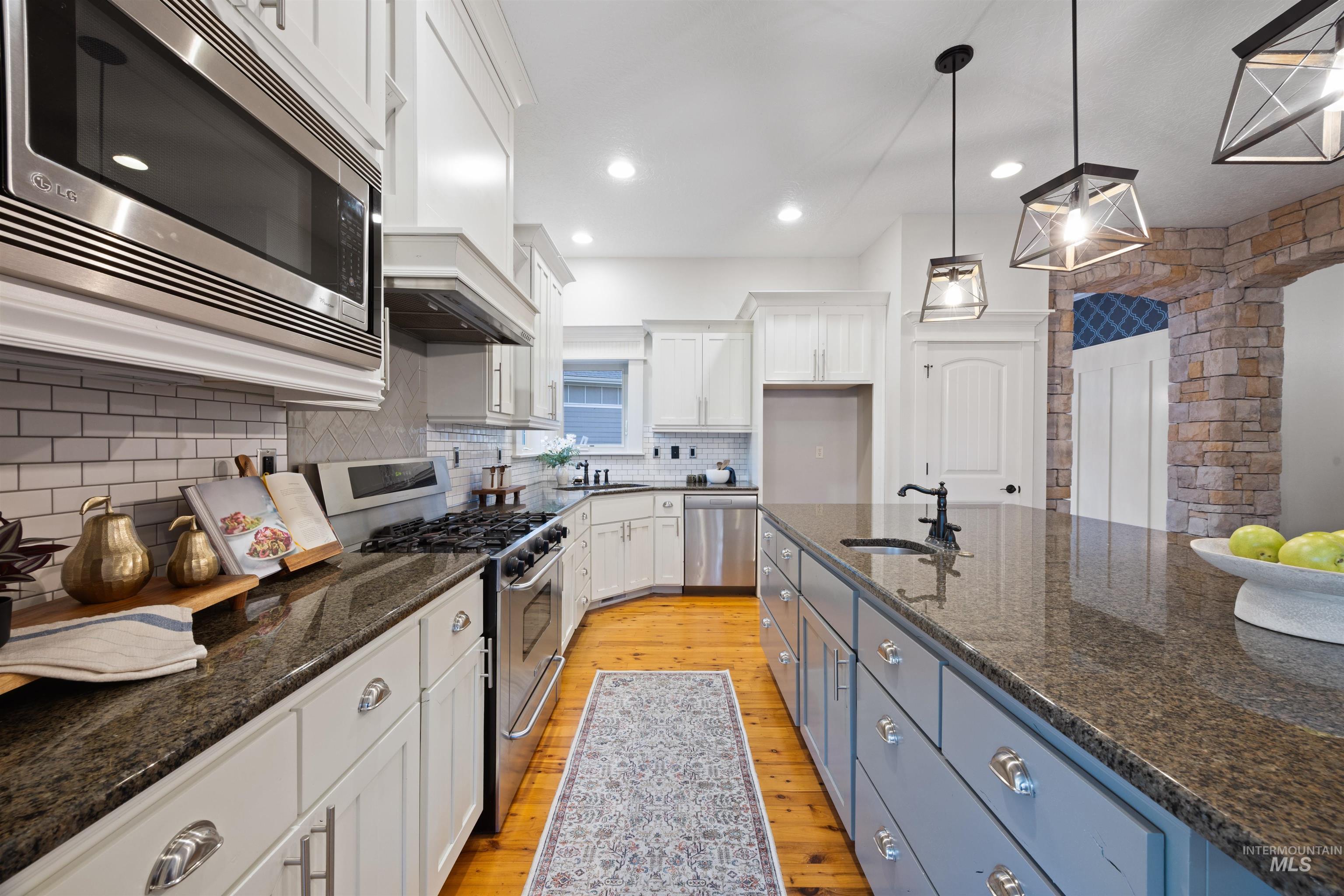 Kitchen with stainless steel appliances, white cabinets, dark stone counters, light wood finished floors, and hanging light fixtures