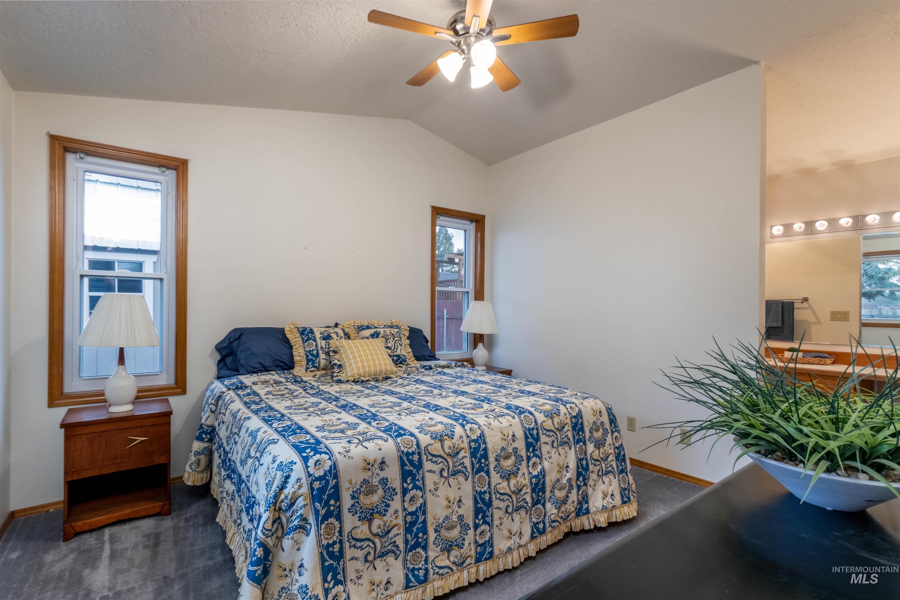 Bedroom featuring vaulted ceiling, multiple windows, dark carpet, and a ceiling fan