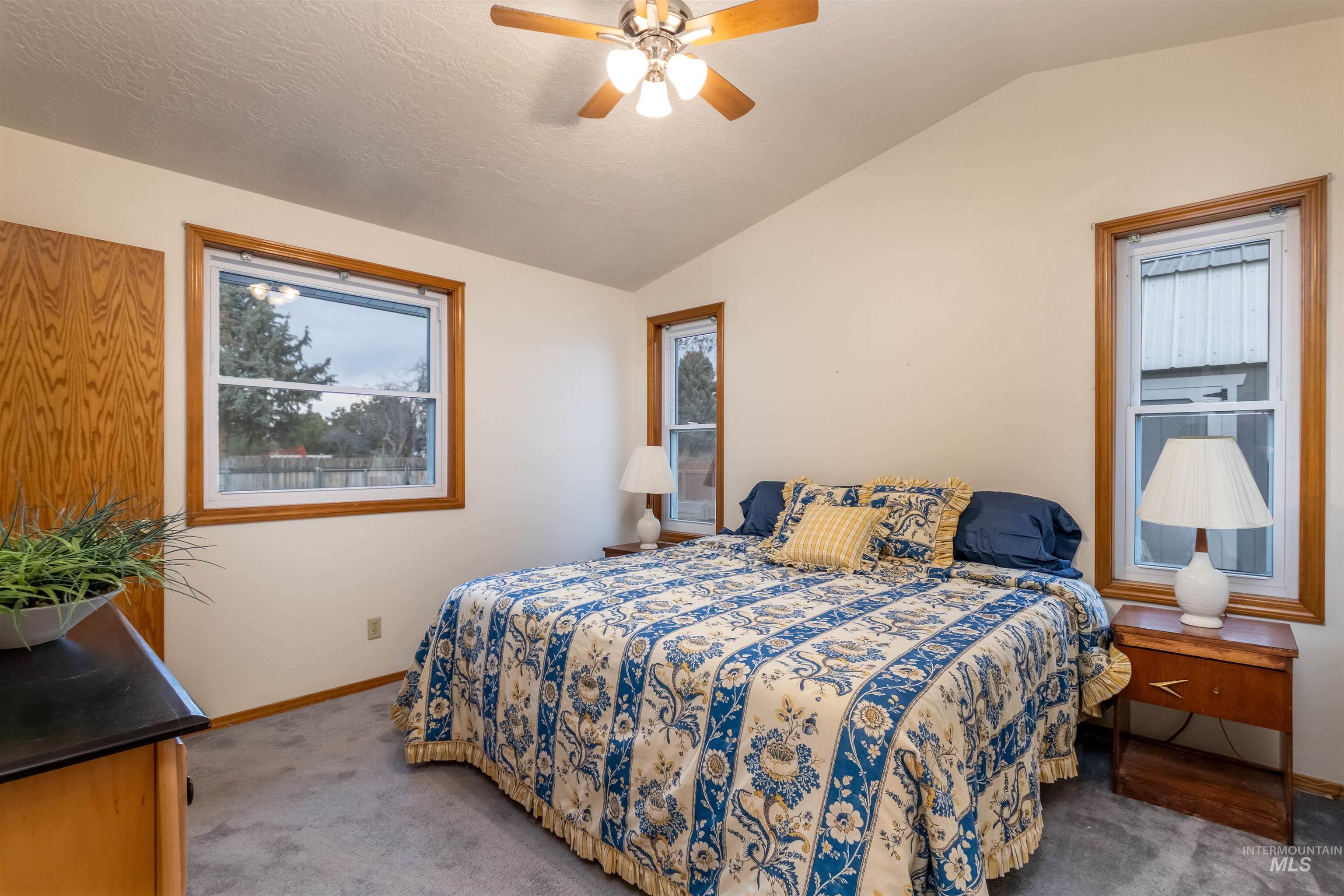 Bedroom with carpet floors, lofted ceiling, multiple windows, a ceiling fan, and a textured ceiling