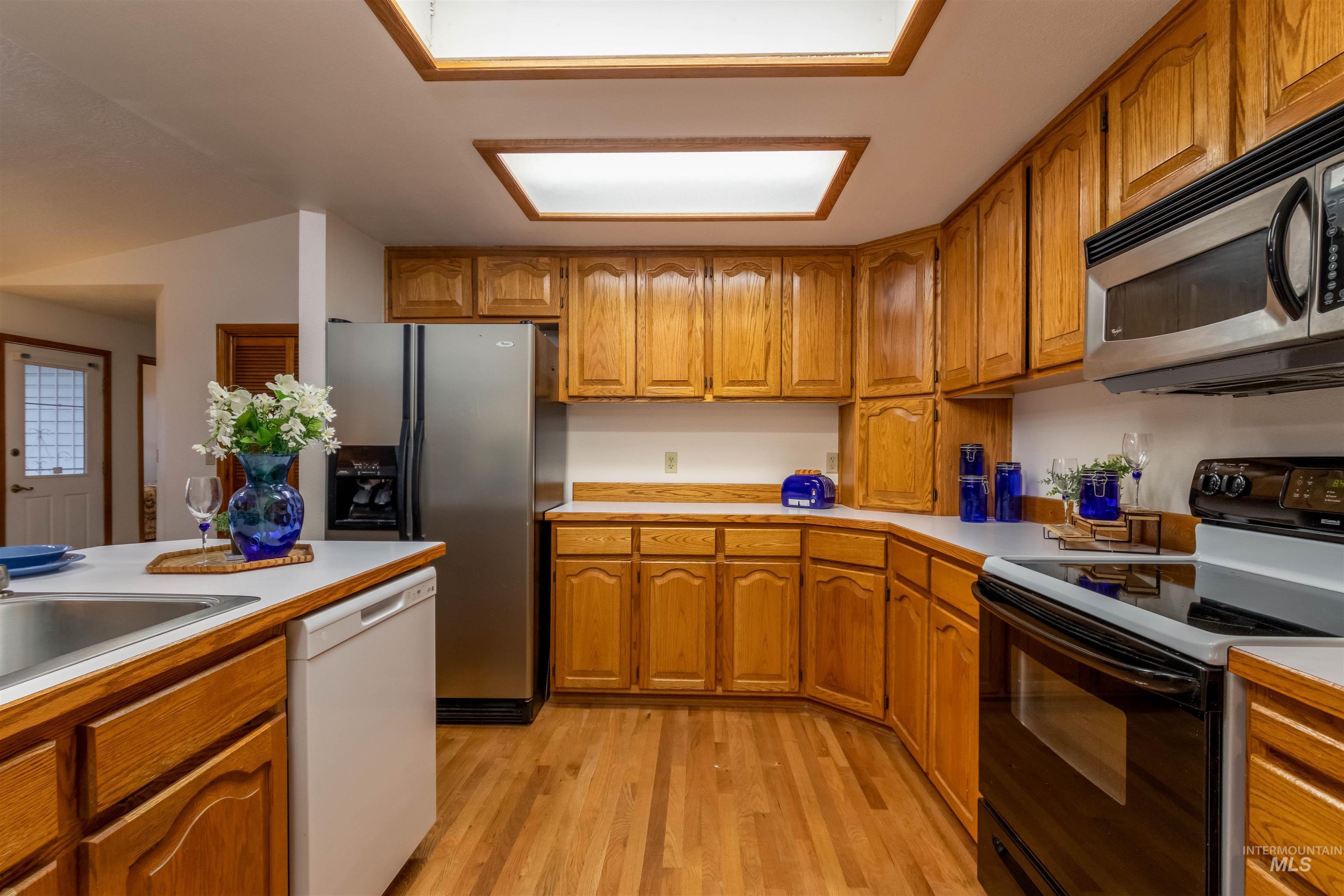 Kitchen with brown cabinets, stainless steel appliances, light countertops, and light wood-style floors