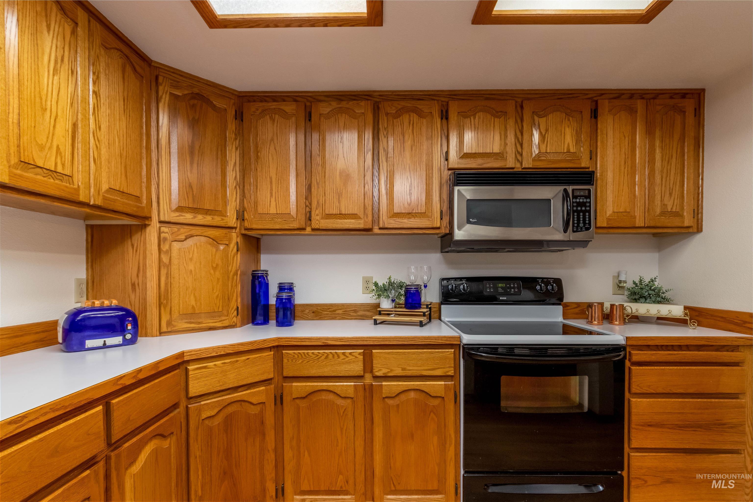 Kitchen with brown cabinets, light countertops, electric range, and stainless steel microwave