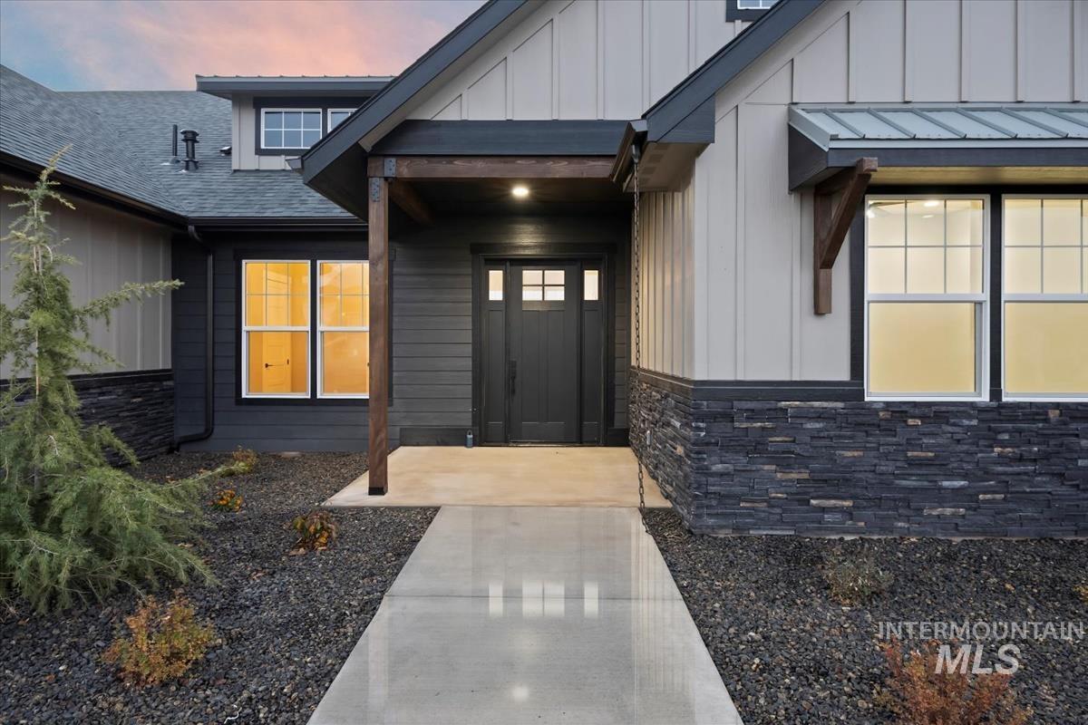 Exterior entry at dusk with board and batten siding, a shingled roof, and stone siding