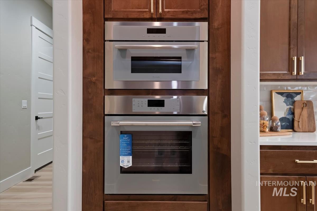 Kitchen view of light countertops, double oven, brown cabinetry, and light wood-style floors