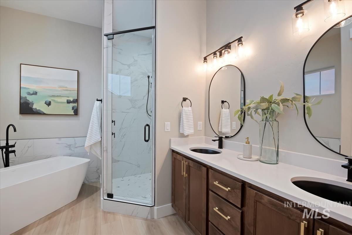 Full bathroom featuring a soaking tub, double vanity, and a marble finish shower