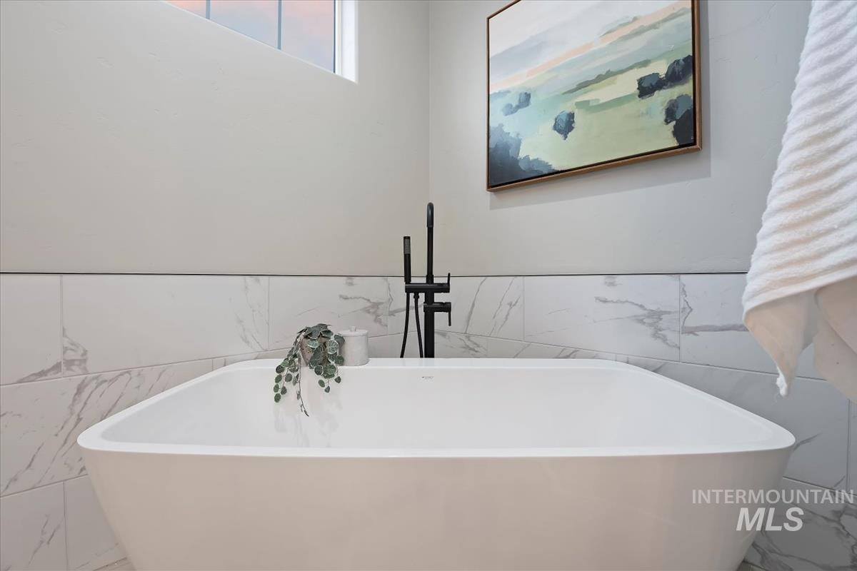 Full bathroom with tile walls, a wainscoted wall, and a soaking tub