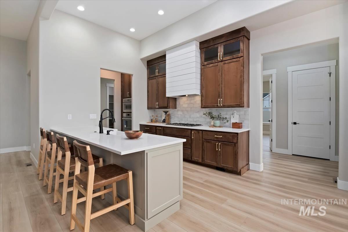Kitchen featuring glass insert cabinets, a breakfast bar area, dark brown cabinets, decorative backsplash, and recessed lighting
