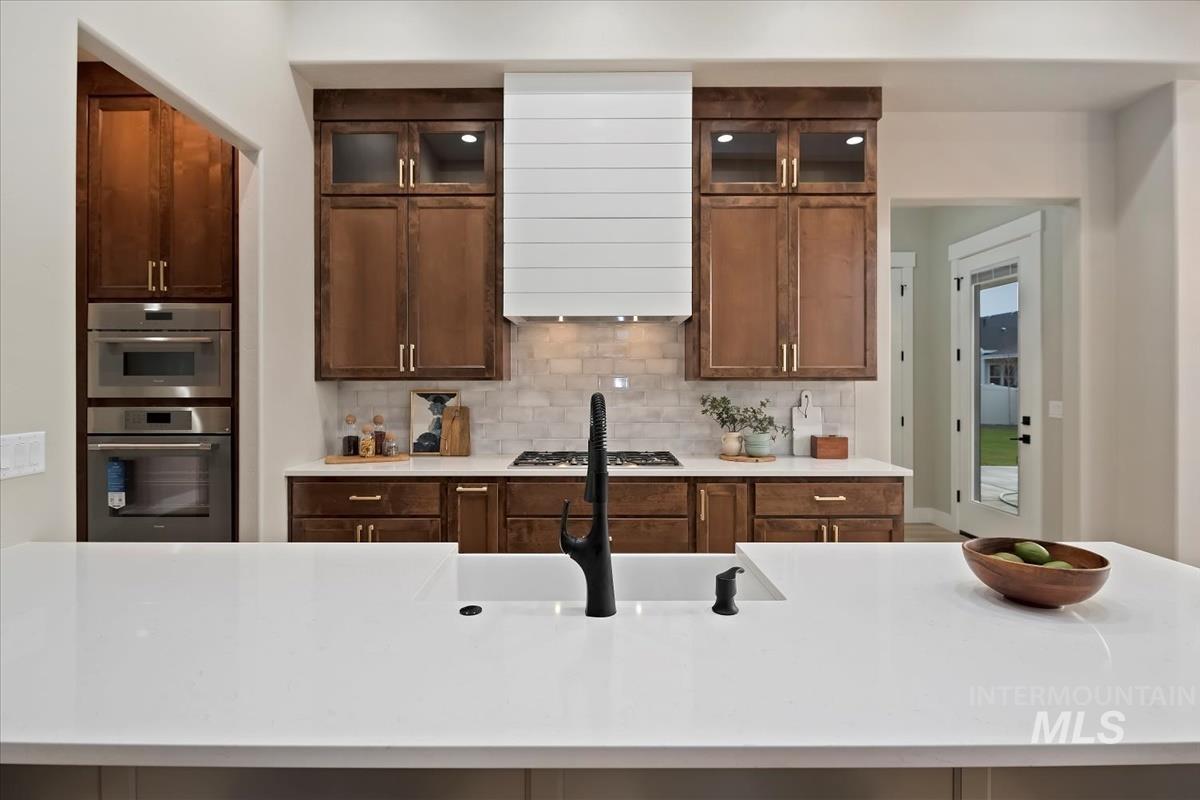 Kitchen featuring light stone counters, glass insert cabinets, backsplash, and an island with sink