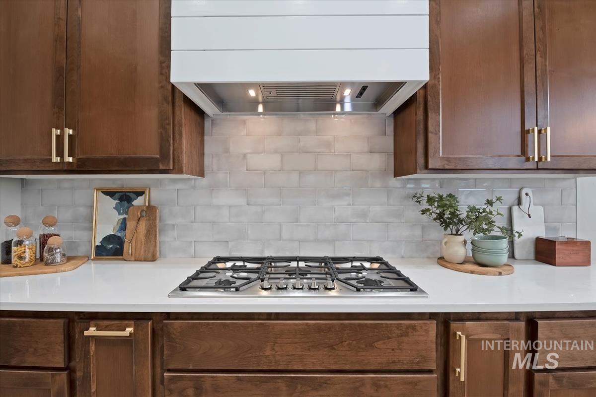 Kitchen with ventilation hood, stainless steel gas cooktop, backsplash, and light stone counters