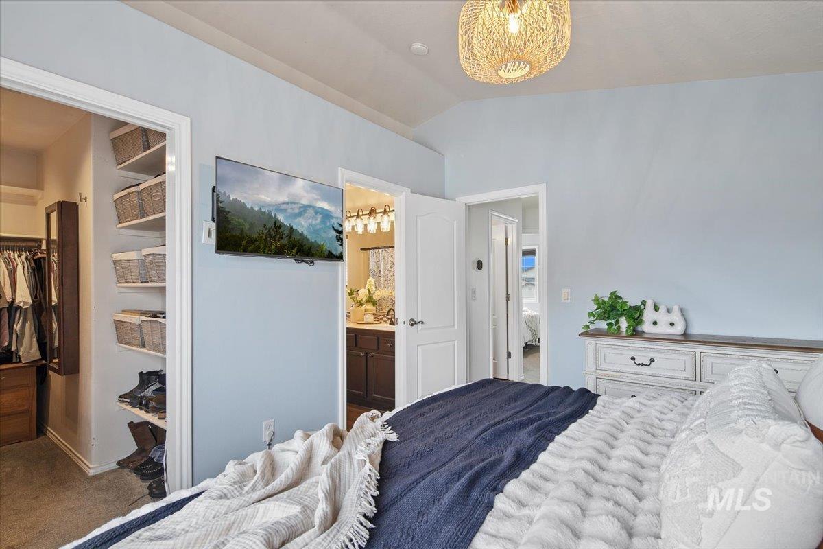 Carpeted bedroom featuring vaulted ceiling, a spacious closet, and ensuite bathroom