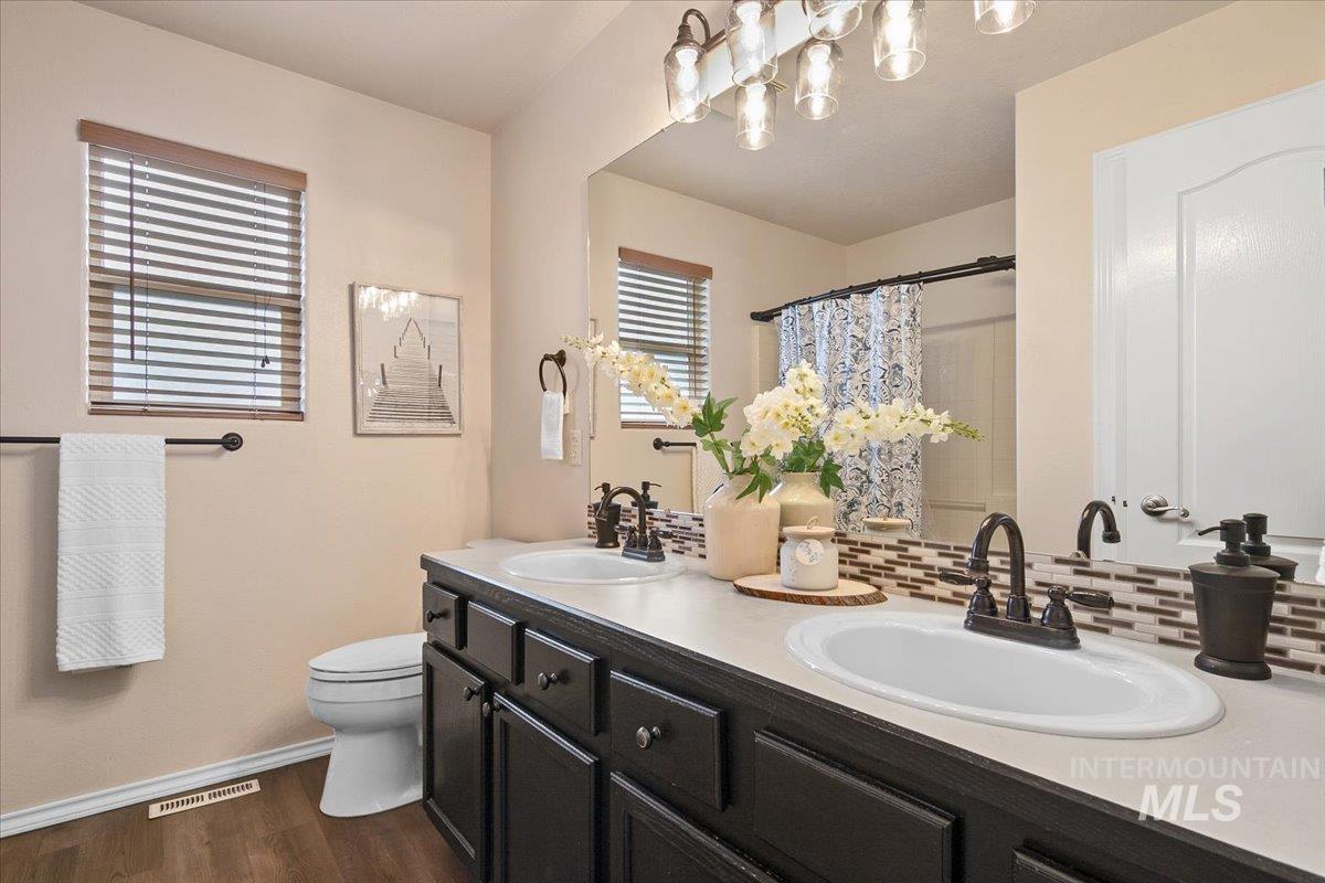 Bathroom with double vanity, a shower with shower curtain, dark wood-style flooring, and decorative backsplash