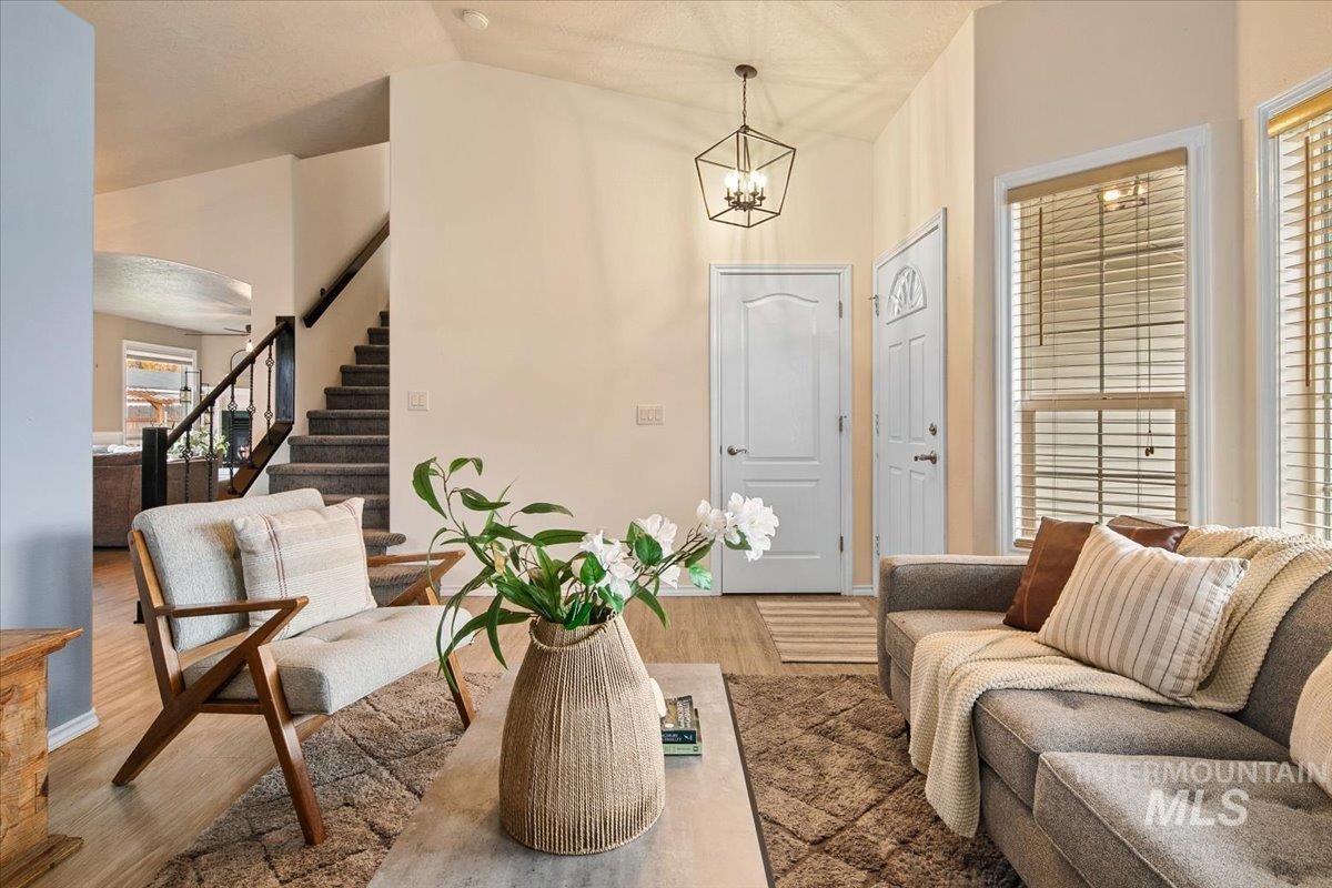 Living area featuring stairs, light wood-type flooring, vaulted ceiling, a chandelier, and arched walkways