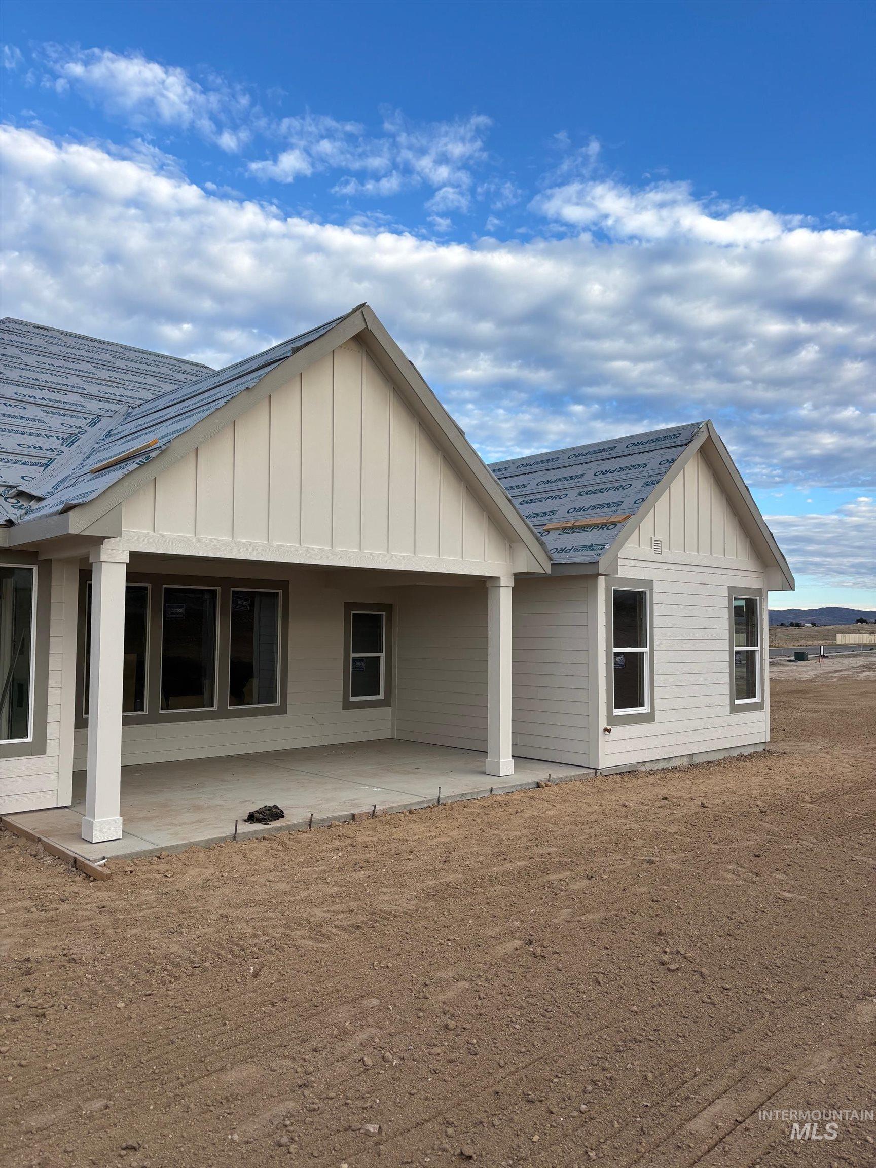 Back of property with board and batten siding, a shingled roof, and a patio area
