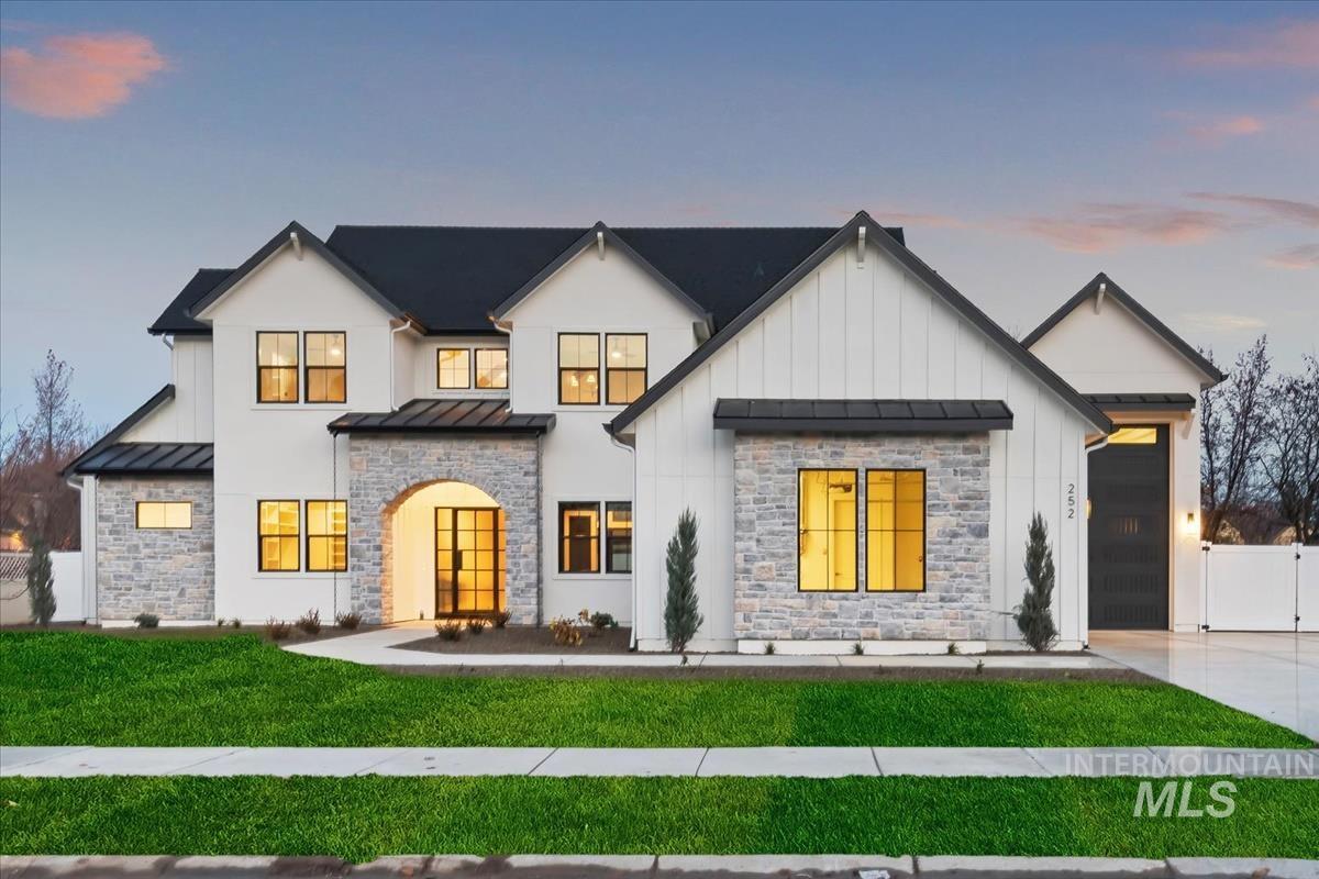 Modern inspired farmhouse with a standing seam roof, a metal roof, driveway, stone siding, and an attached garage