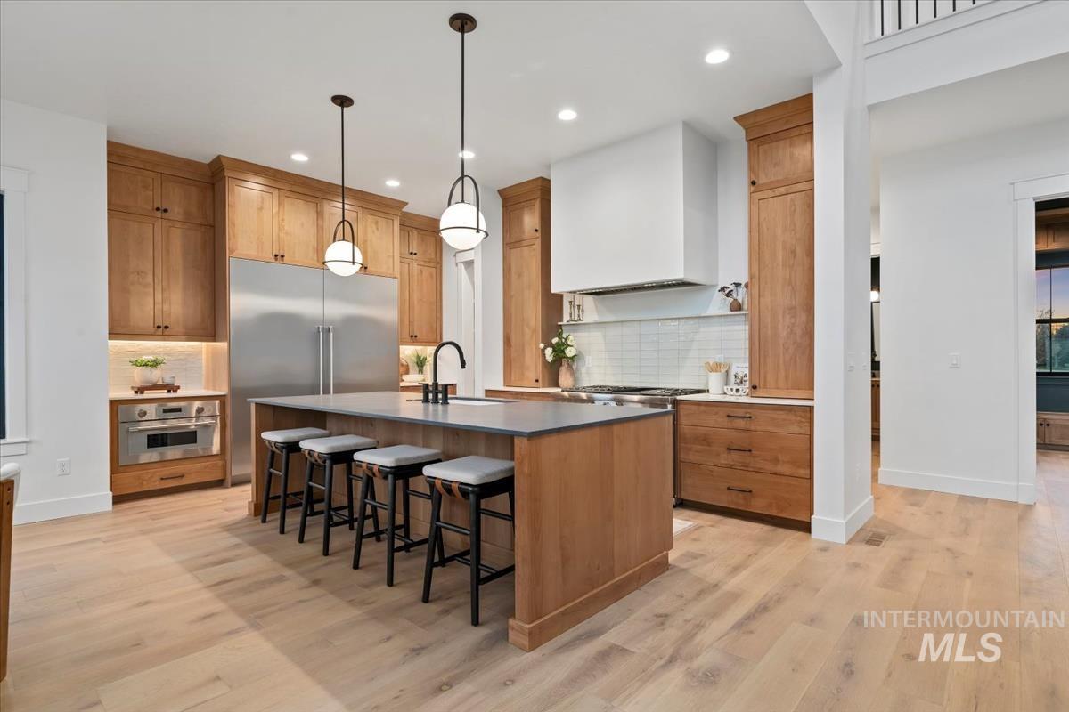 Kitchen featuring a center island with sink, a breakfast bar area, hanging light fixtures, appliances with stainless steel finishes, and brown cabinets