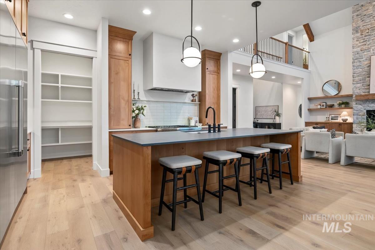 Kitchen with brown cabinets, tasteful backsplash, built in fridge, an island with sink, and a high ceiling