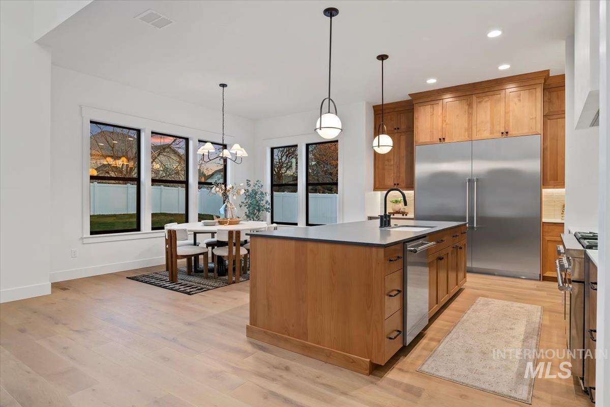 Kitchen featuring brown cabinetry, high end appliances, pendant lighting, light wood-style floors, and recessed lighting