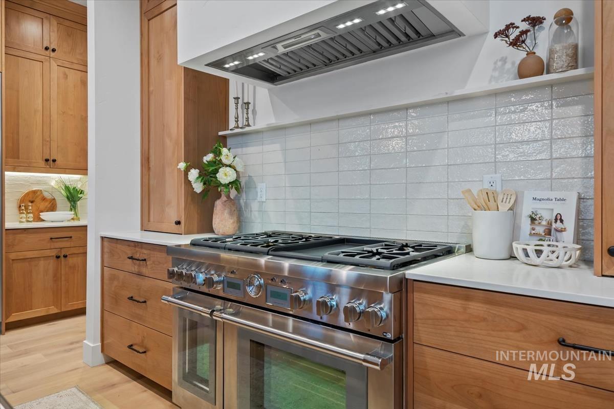 Kitchen featuring custom range hood, double oven range, backsplash, brown cabinets, and light wood-style flooring