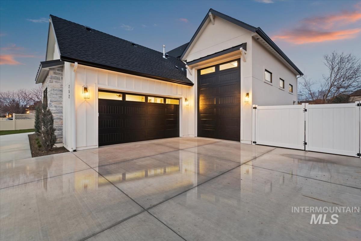 View of front facade with stone siding, a garage, driveway, a shingled roof, and a gate