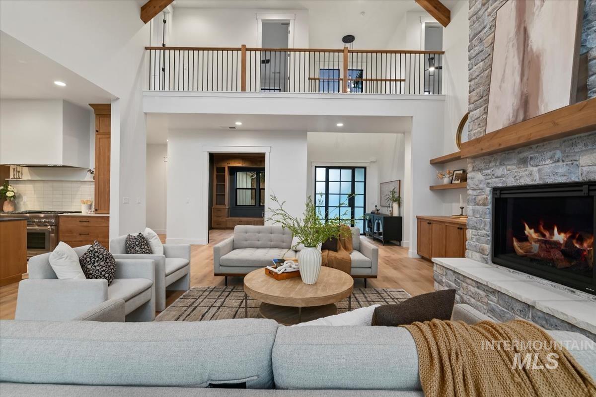 Living room featuring a high ceiling, light wood-style flooring, a stone fireplace, and recessed lighting