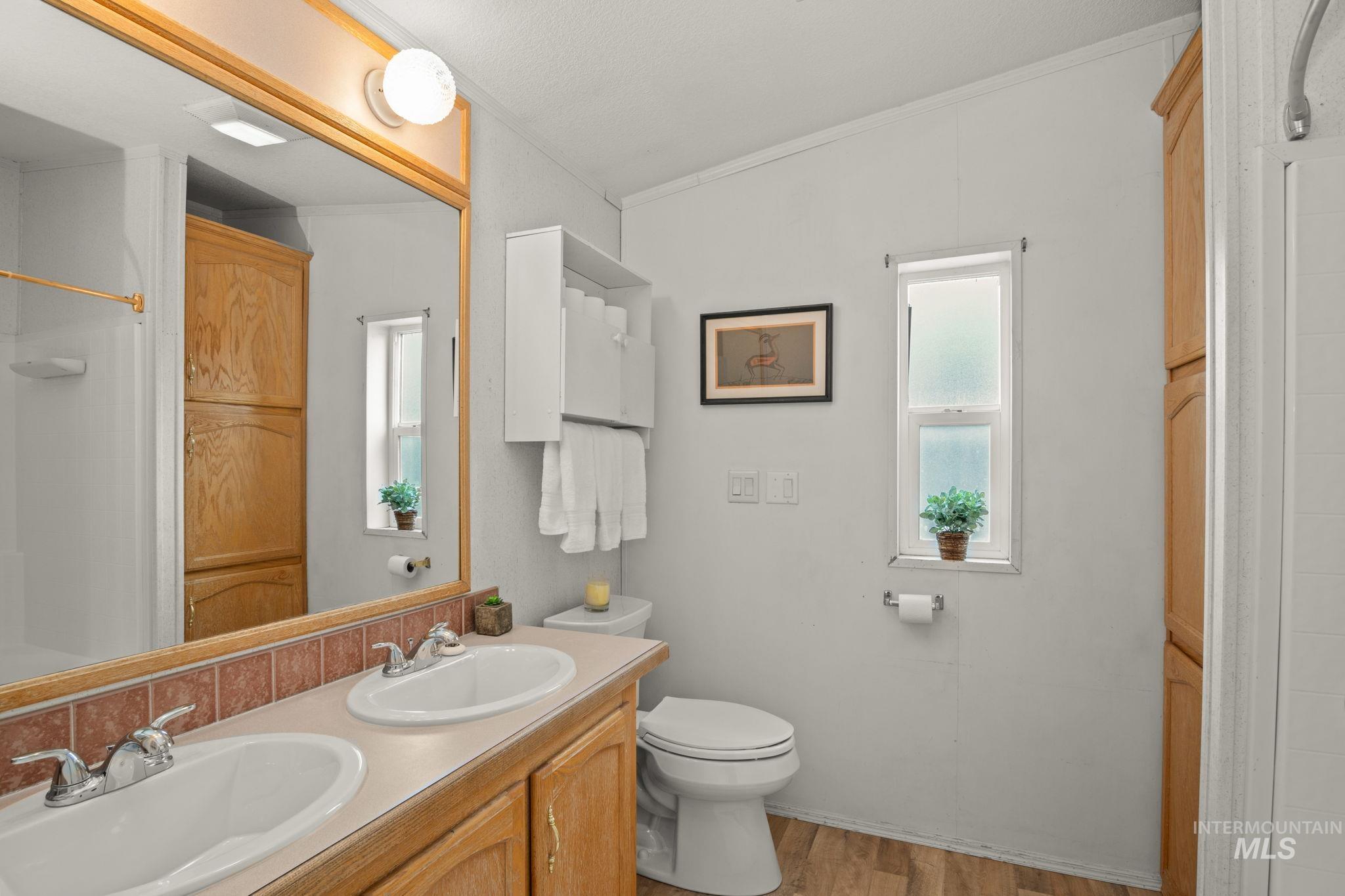 Bathroom featuring double vanity, light wood finished floors, curtained shower, and crown molding