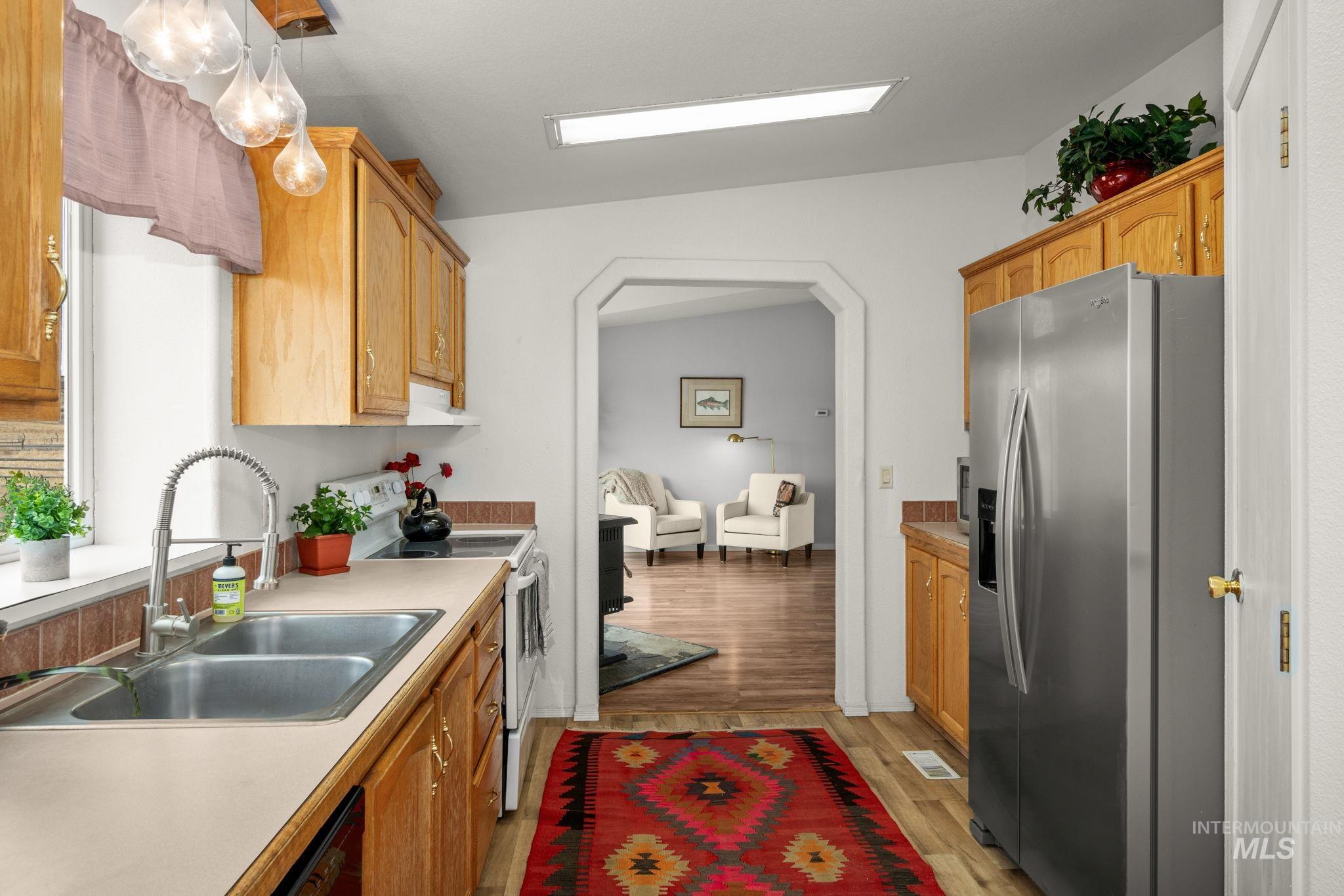 Kitchen with stainless steel refrigerator with ice dispenser, electric stove, light wood-type flooring, light countertops, and arched walkways