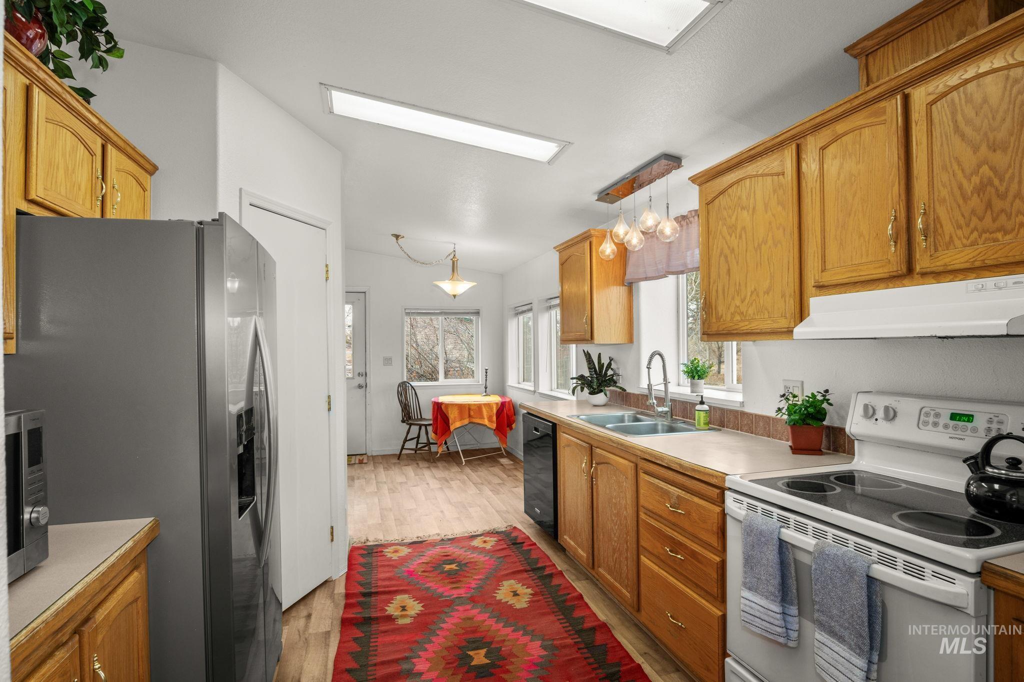 Kitchen with stainless steel appliances, pendant lighting, brown cabinetry, light wood-style floors, and under cabinet range hood