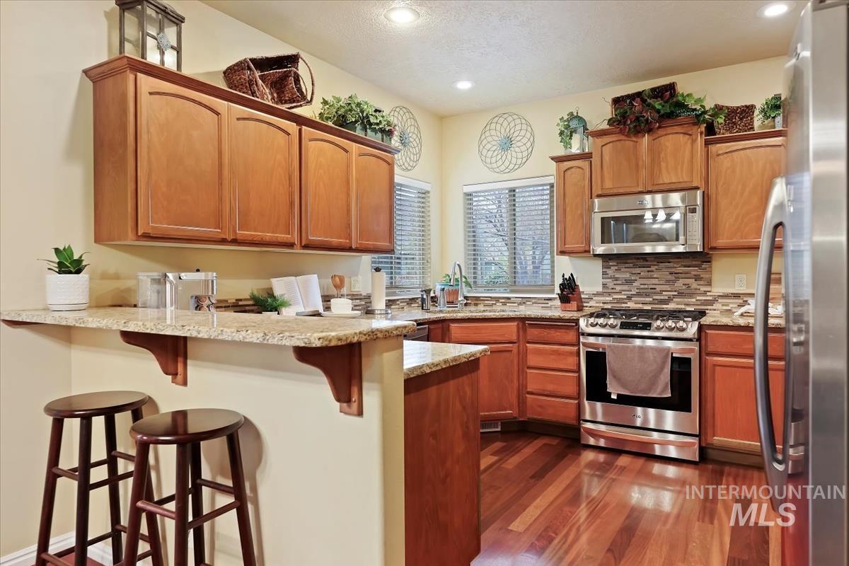 Kitchen featuring a peninsula, stainless steel appliances, brown cabinetry, light stone counters, and recessed lighting