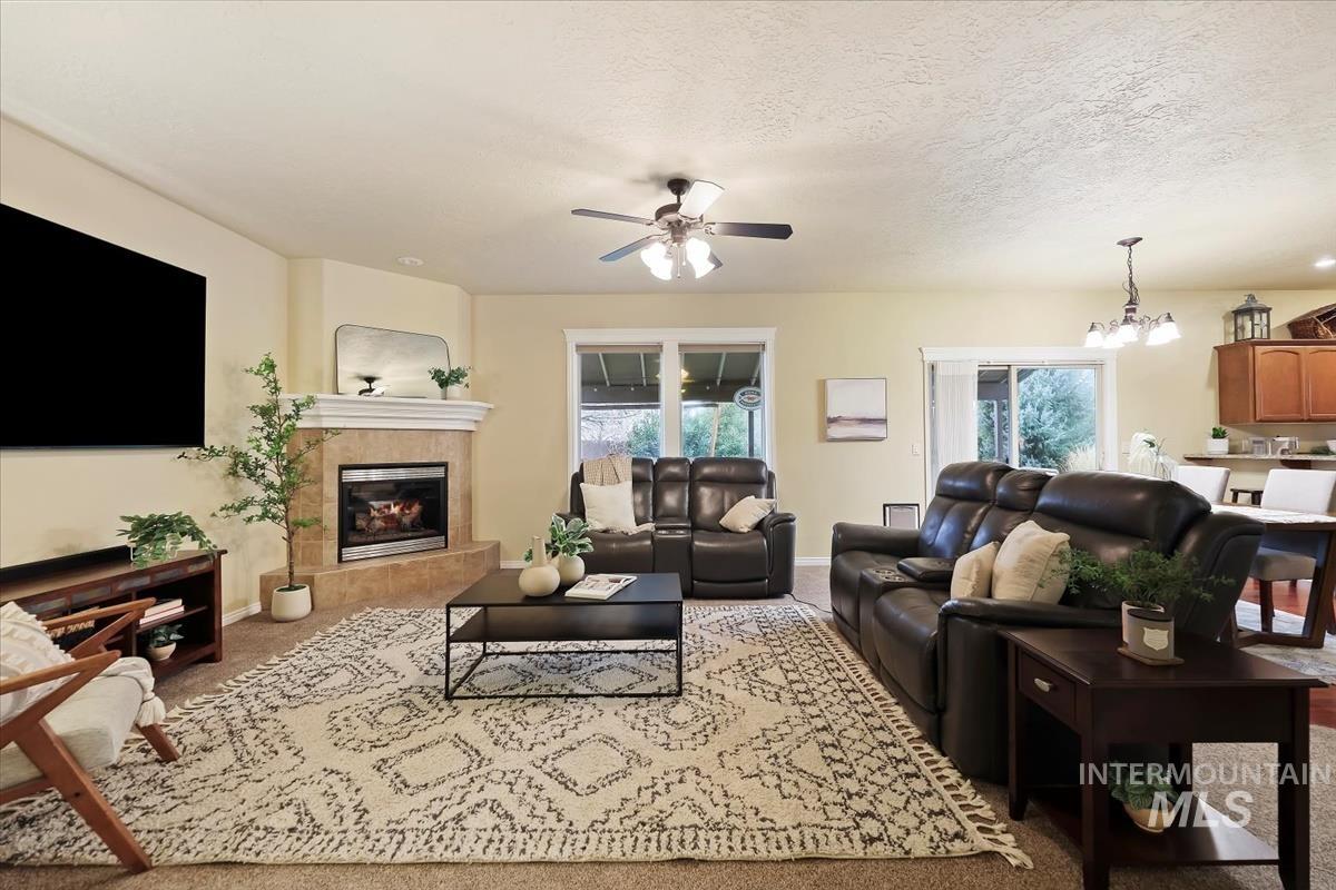 Carpeted living area with a chandelier, a textured ceiling, a fireplace, and ceiling fan