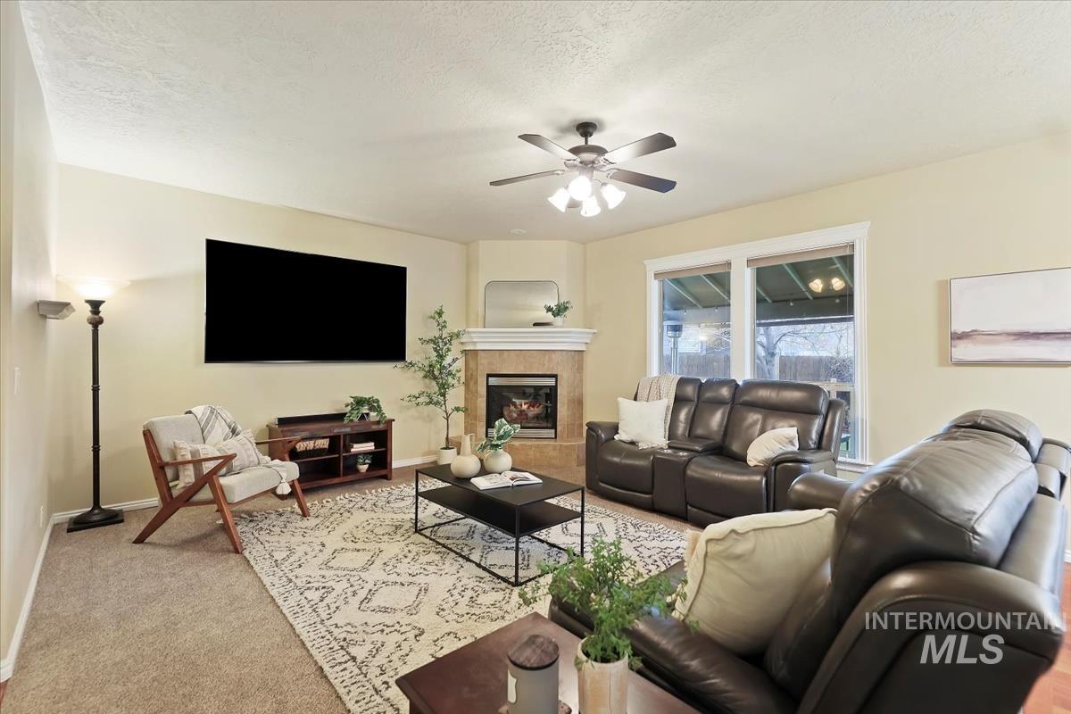 Carpeted living room featuring a tile fireplace, a textured ceiling, and ceiling fan