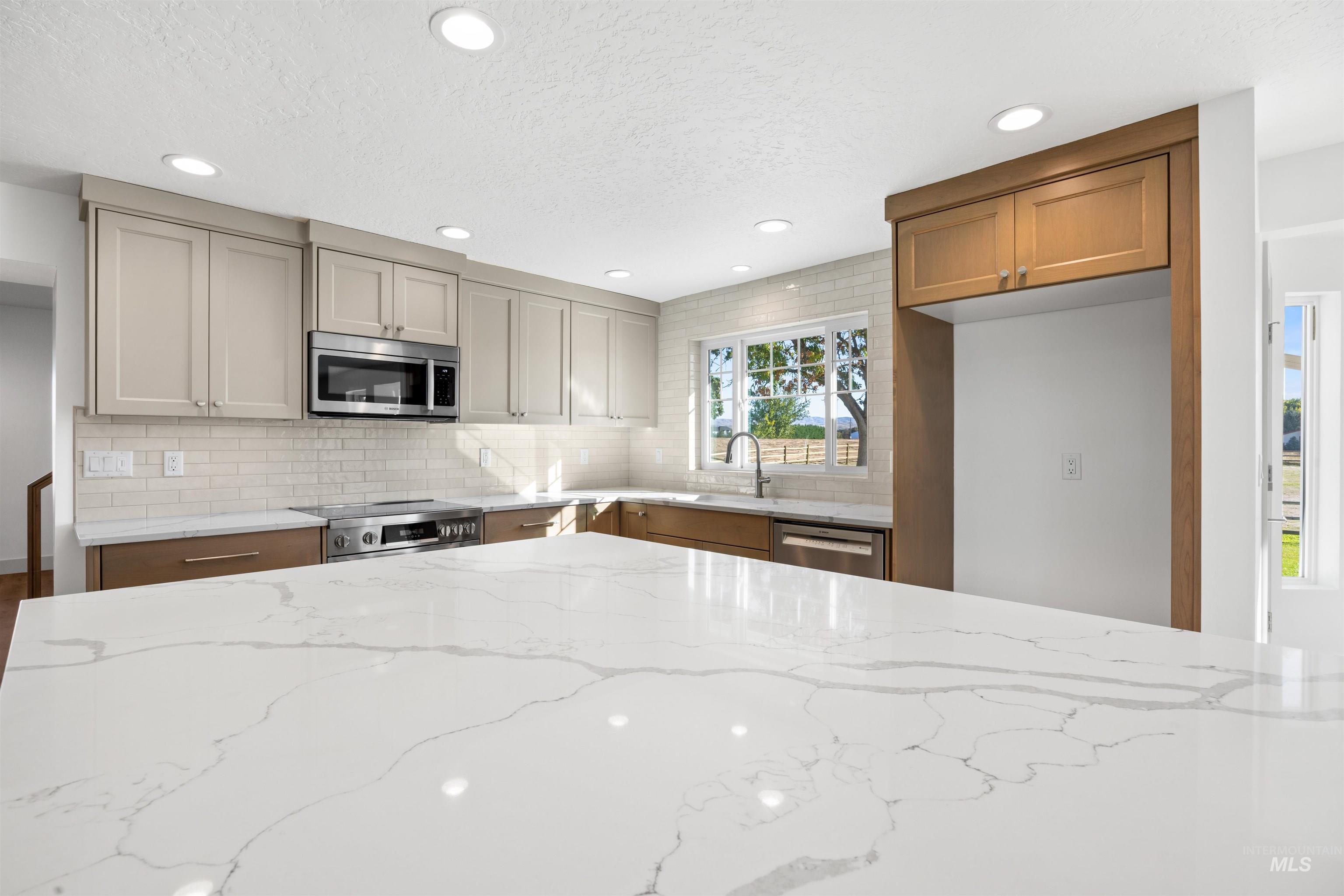 Kitchen featuring light stone countertops, appliances with stainless steel finishes, recessed lighting, backsplash, and a textured ceiling
