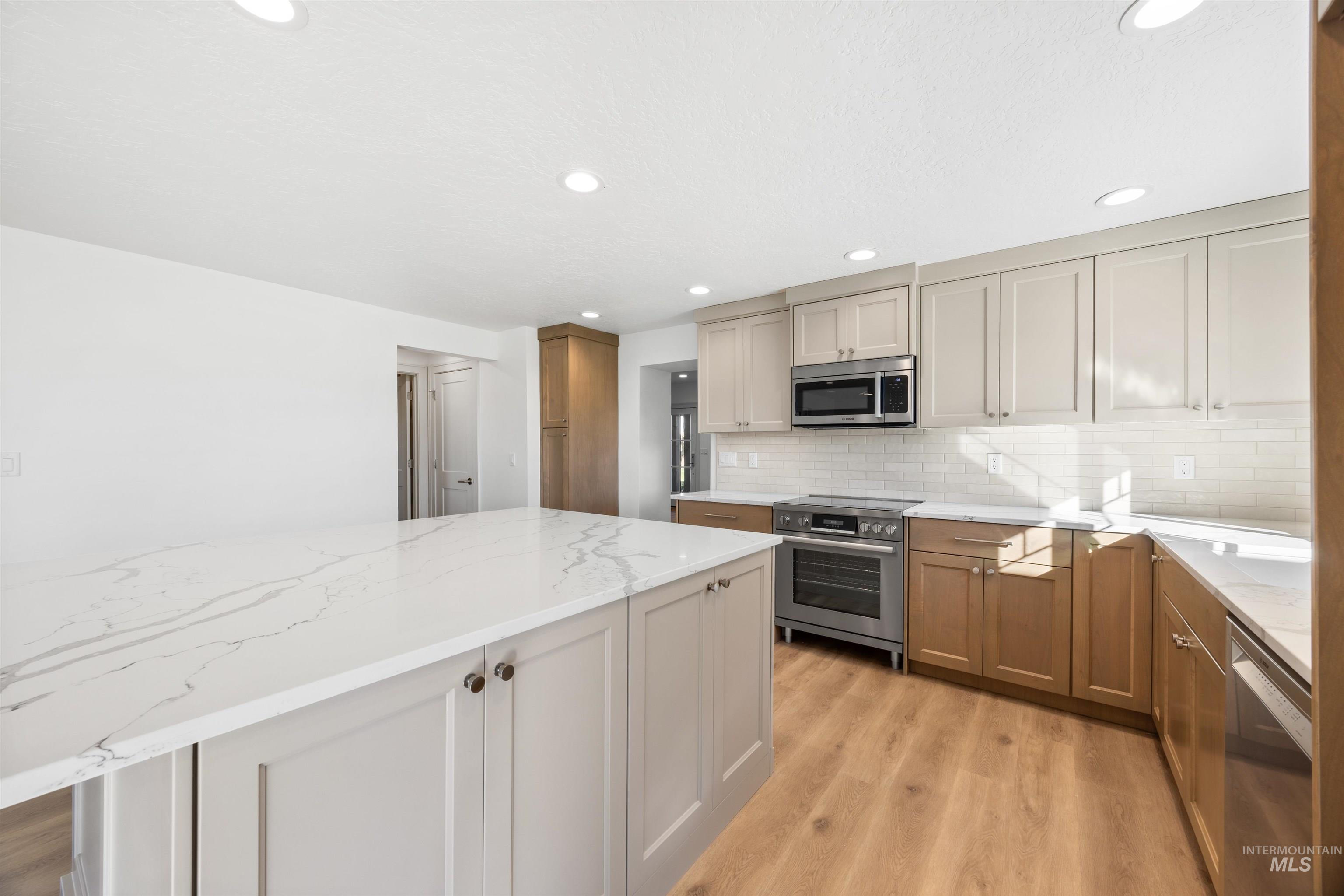 Kitchen with stainless steel appliances, light stone counters, light wood-style floors, decorative backsplash, and recessed lighting