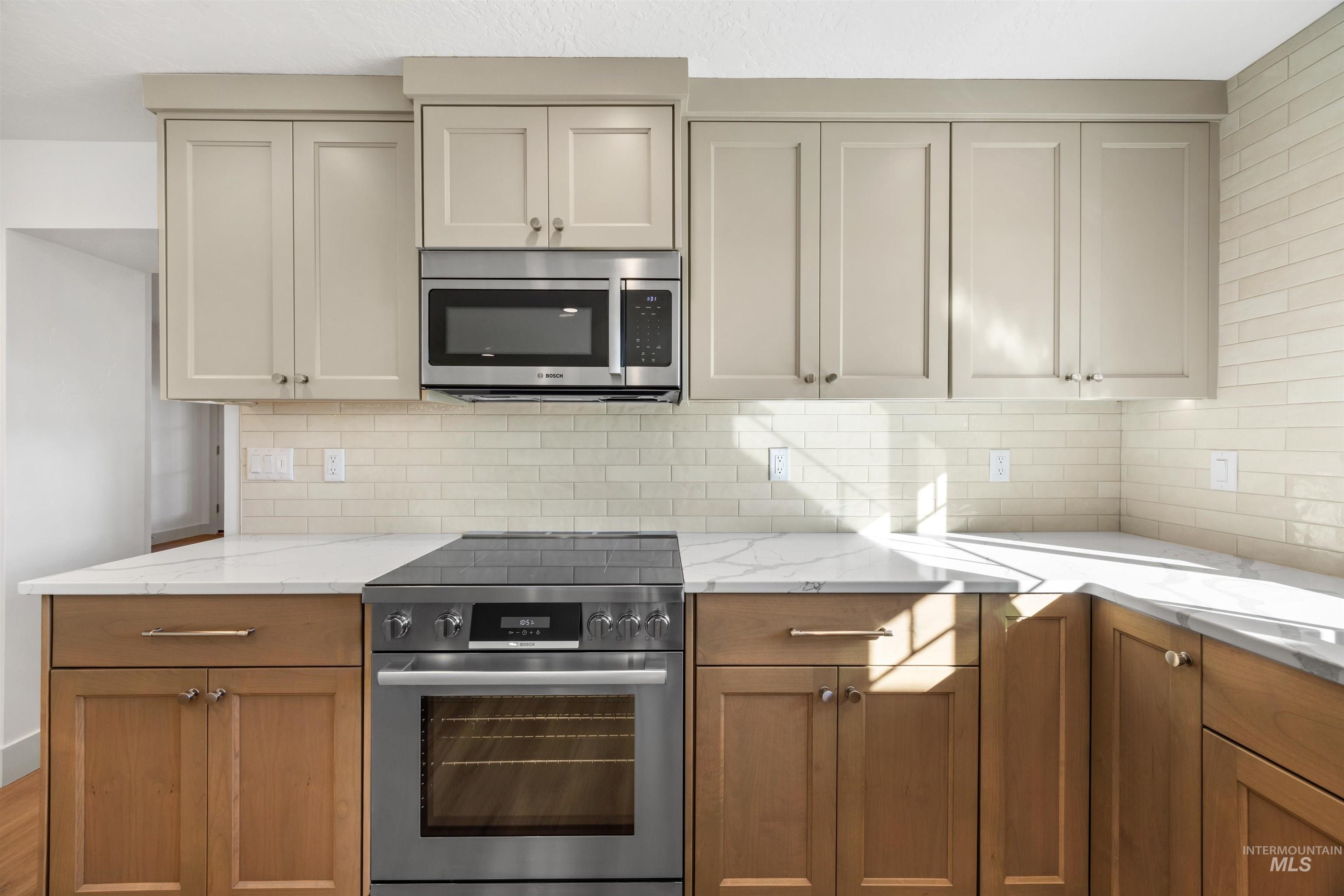 Kitchen featuring stainless steel appliances, light stone countertops, decorative backsplash, and brown cabinets
