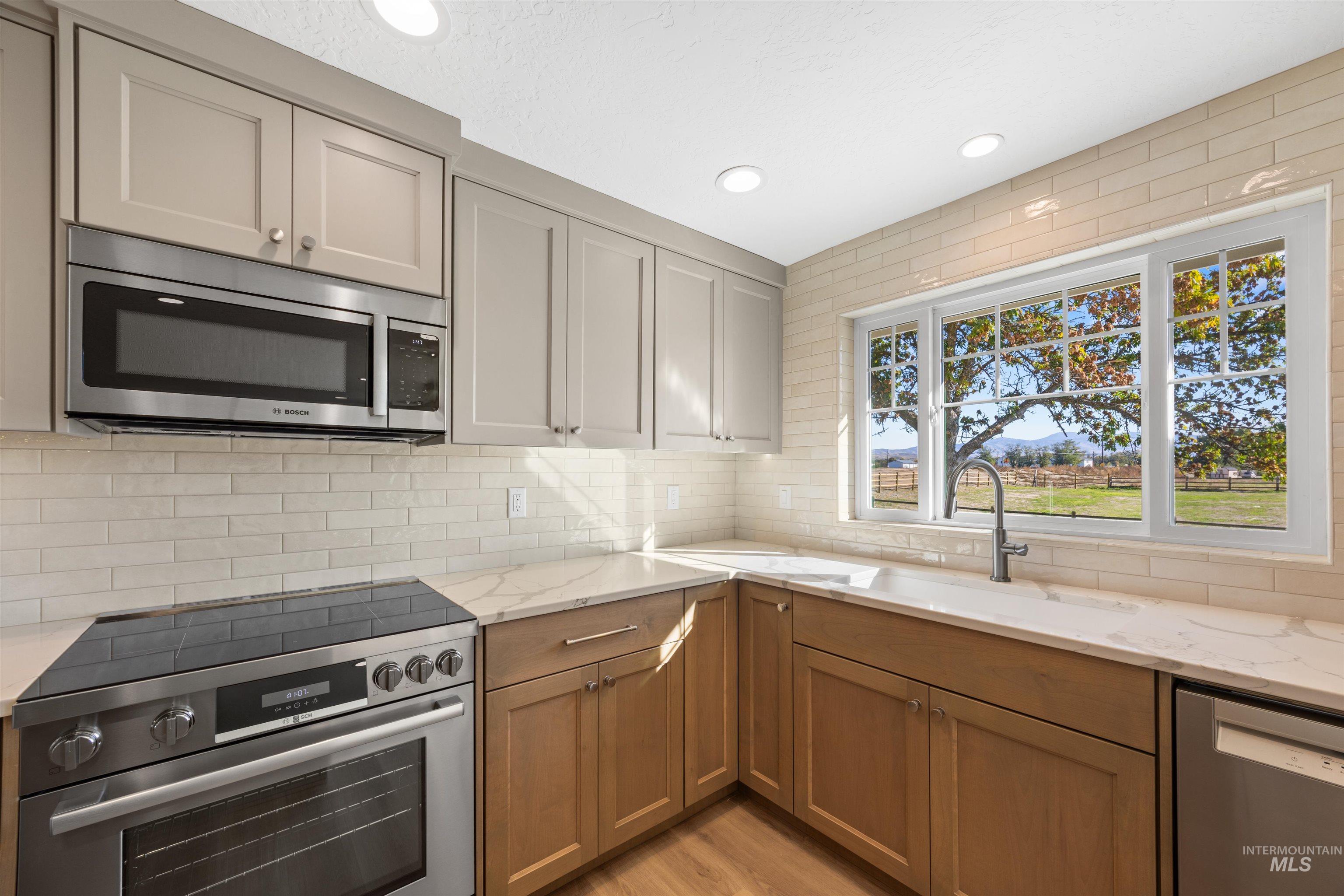 Kitchen featuring appliances with stainless steel finishes, light stone counters, backsplash, recessed lighting, and light wood-style floors