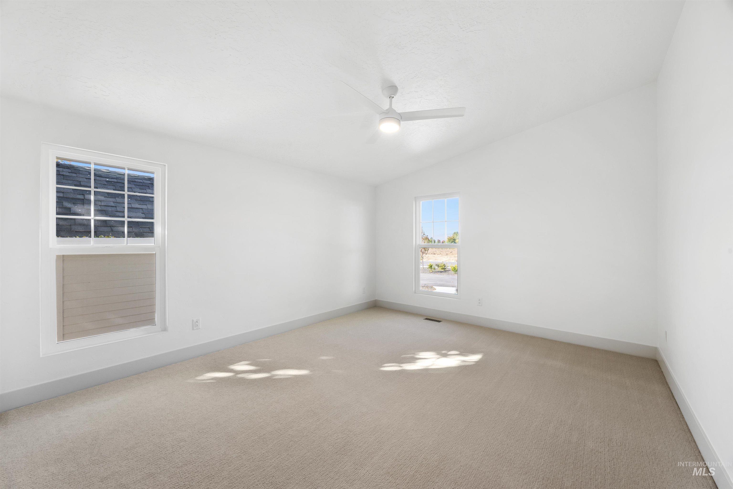 Carpeted spare room featuring vaulted ceiling and ceiling fan