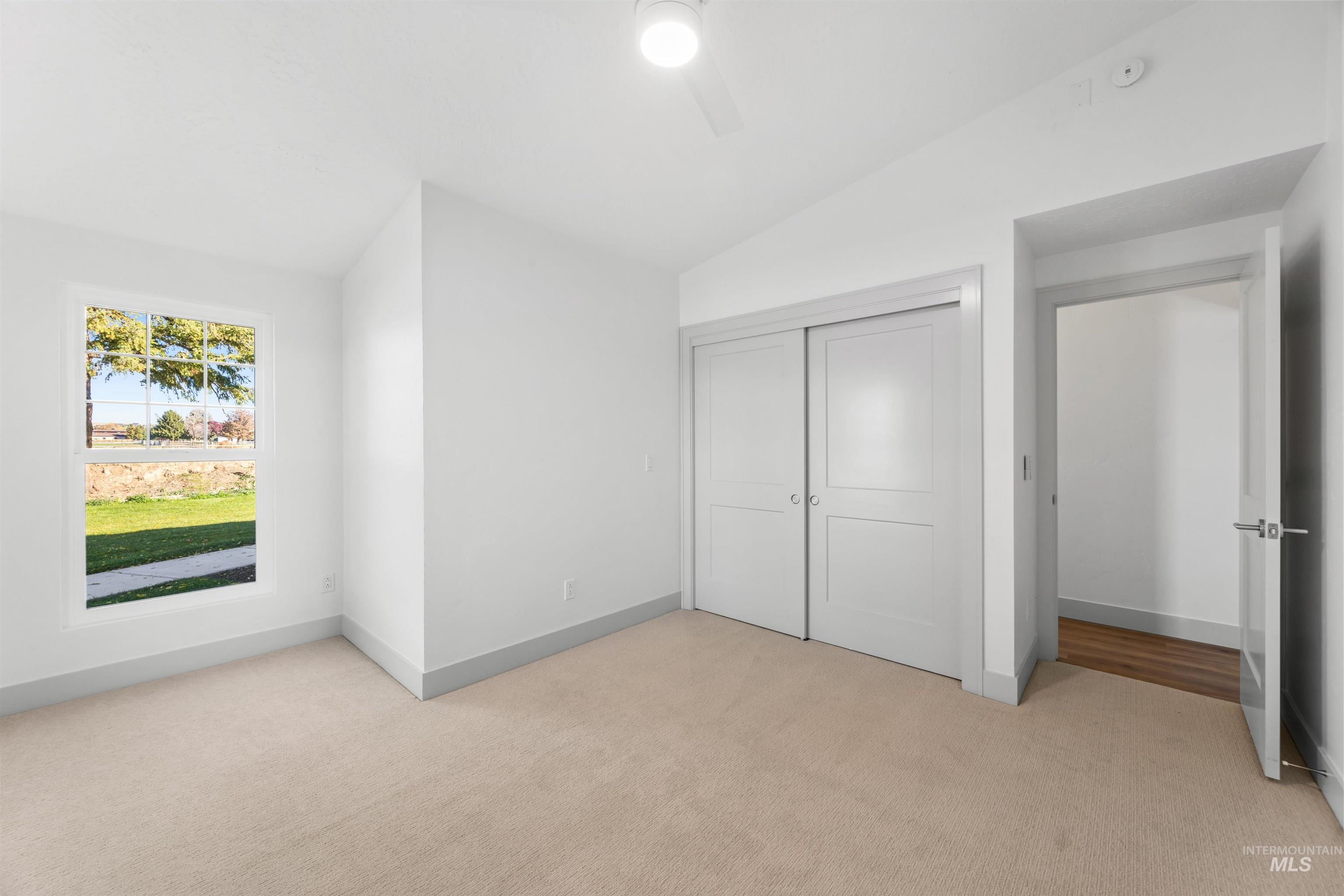 Unfurnished bedroom featuring vaulted ceiling, light carpet, a closet, and ceiling fan