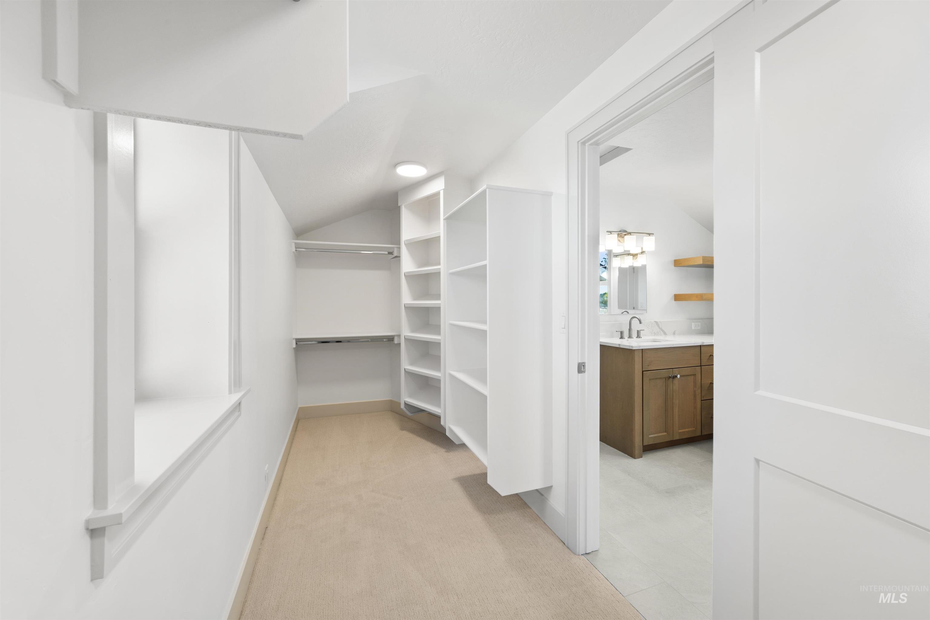 Walk in closet with light colored carpet and lofted ceiling