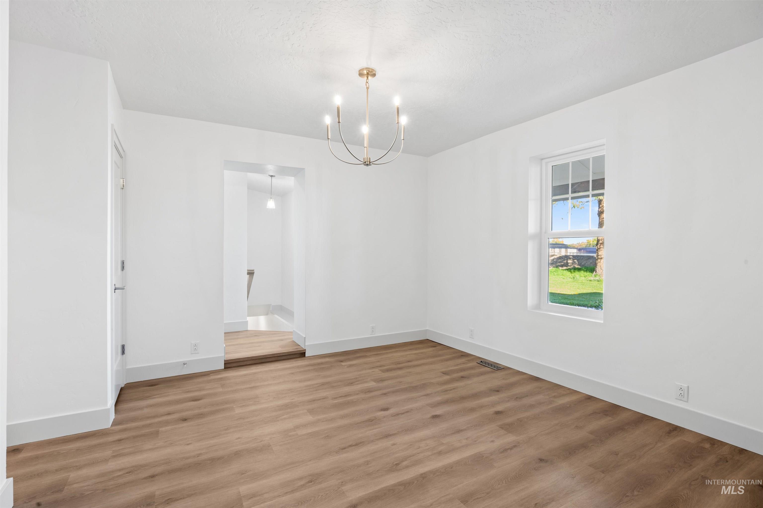 Unfurnished dining area with light wood finished floors, a chandelier, and a textured ceiling