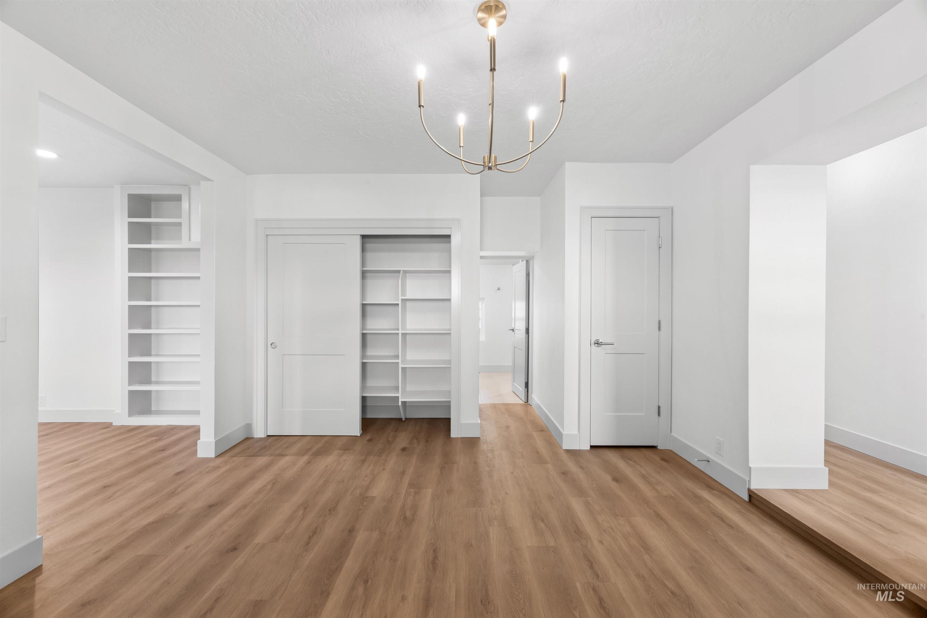 Unfurnished bedroom featuring a chandelier, light wood-style flooring, a closet, and a textured ceiling