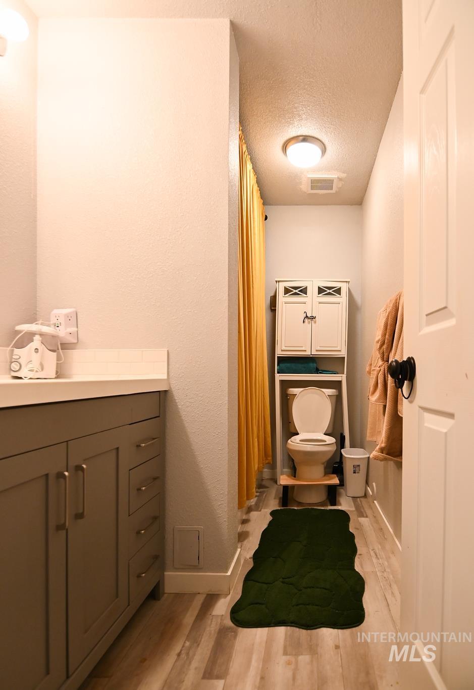 Bathroom featuring vanity, light wood-type flooring, a textured ceiling, curtained shower, and a textured wall