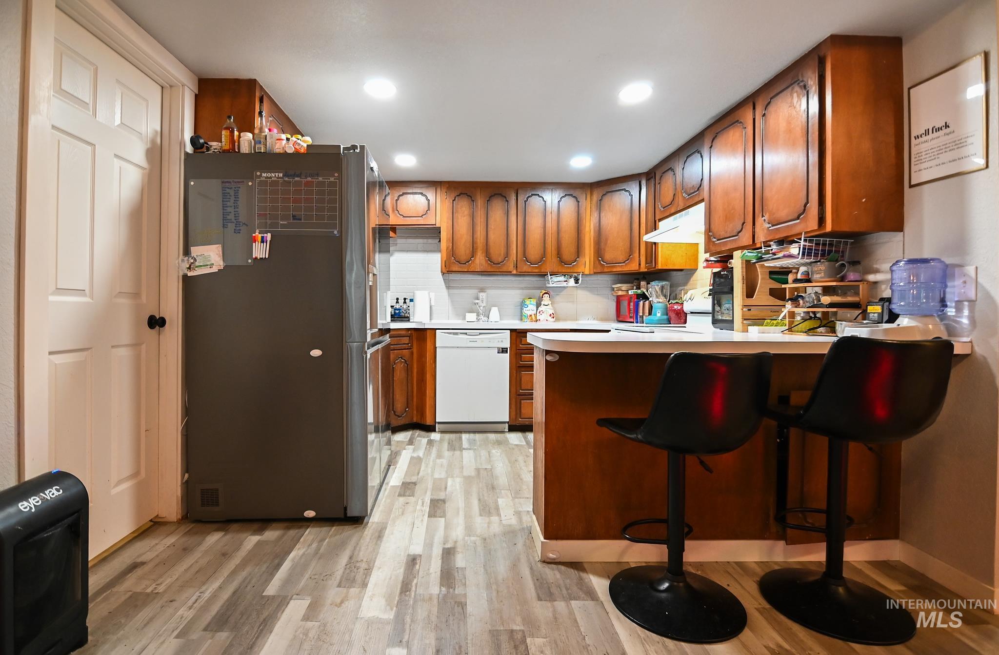 Kitchen with brown cabinetry, freestanding refrigerator, light countertops, a peninsula, and recessed lighting