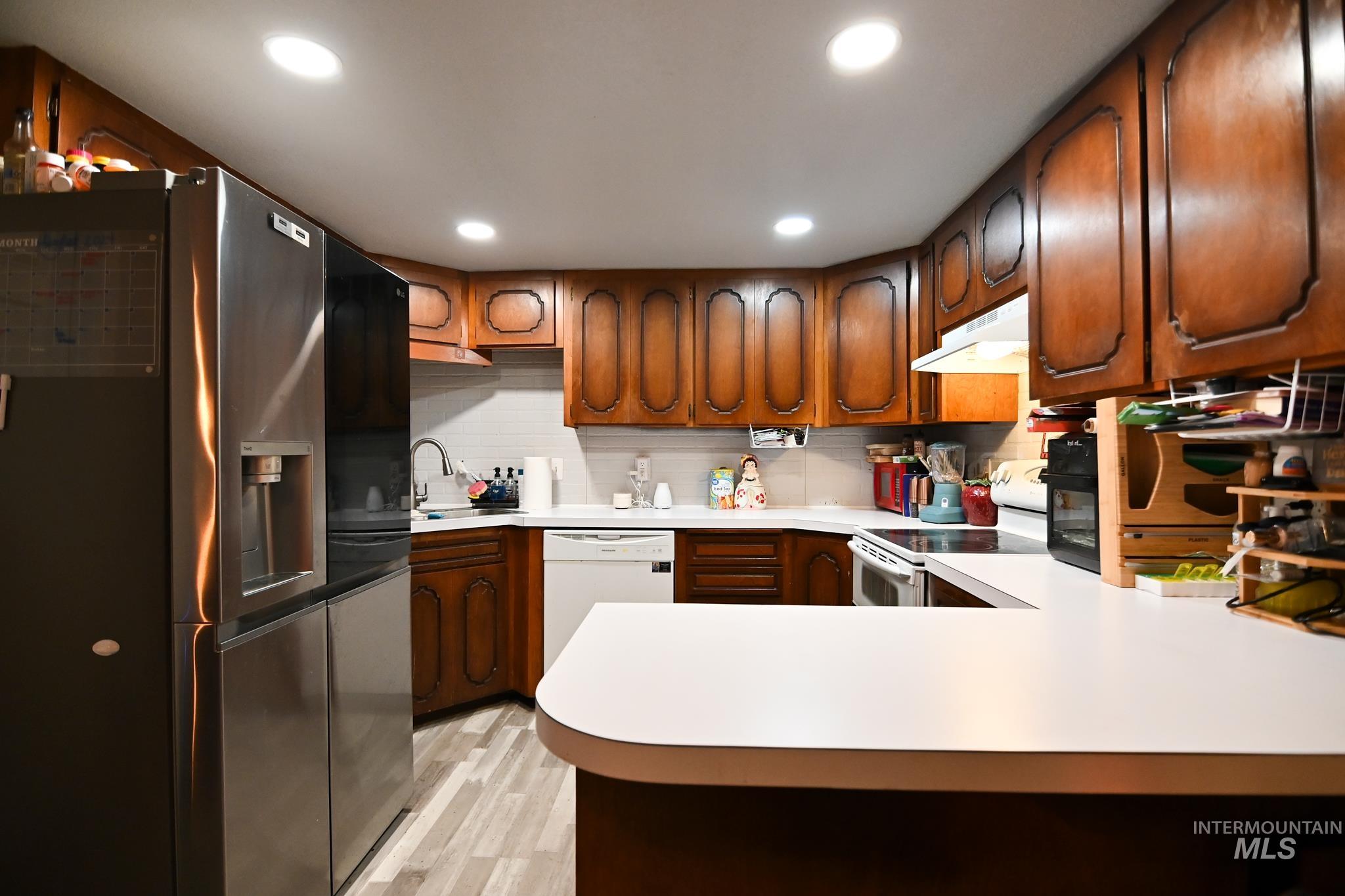 Kitchen with white appliances, a peninsula, light countertops, light wood finished floors, and brown cabinets