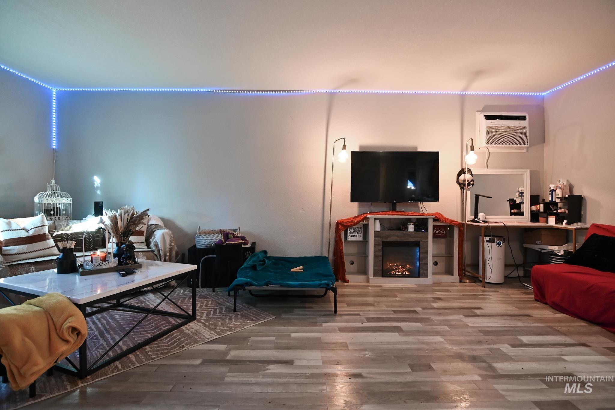 Living room with wood finished floors, a lit fireplace, and an AC wall unit