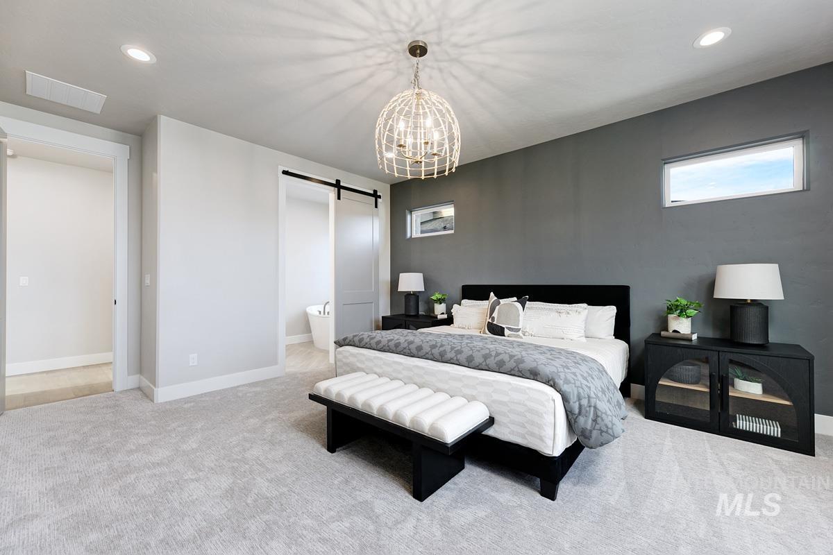 Carpeted bedroom with a barn door, recessed lighting, a chandelier, and ensuite bath