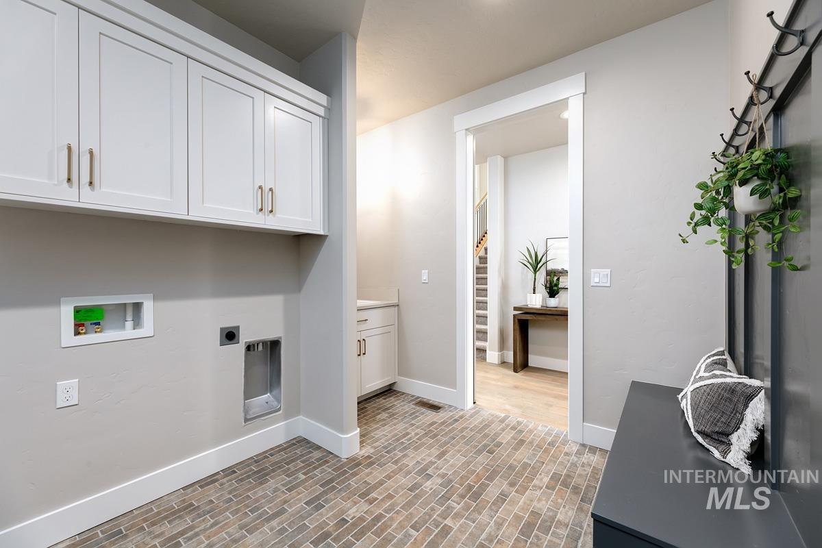 Laundry room featuring brick floors, cabinet space, hookup for a washing machine, and electric dryer hookup