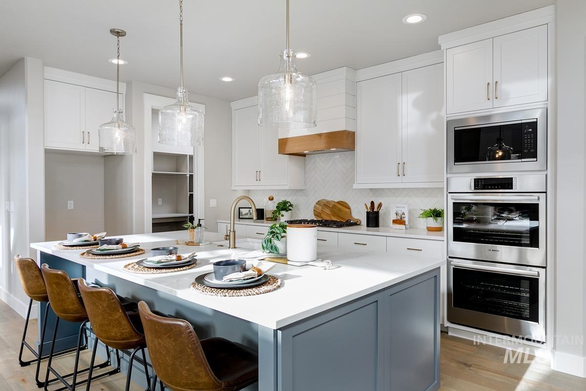 Kitchen featuring white cabinetry, backsplash, appliances with stainless steel finishes, hanging light fixtures, and light wood-type flooring