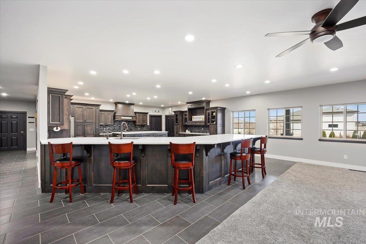 Kitchen with decorative backsplash, a breakfast bar area, recessed lighting, dark brown cabinetry, and premium range hood