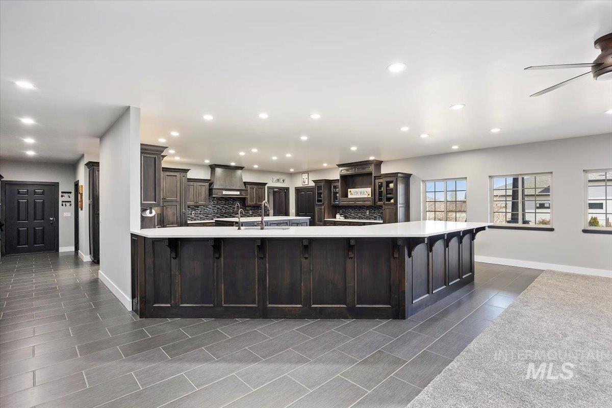 Kitchen with custom exhaust hood, recessed lighting, glass insert cabinets, ceiling fan, and a kitchen bar