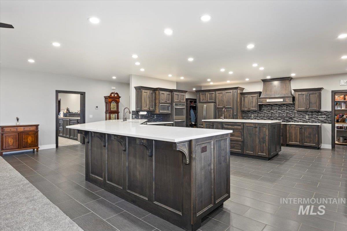 Kitchen featuring a breakfast bar area, recessed lighting, premium range hood, dark brown cabinets, and backsplash
